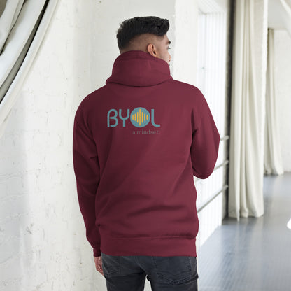 A young man wearing a maroon "BYOL: a mindset" hoodie, viewed from the back. The hoodie features the "BYOL" logo in teal and yellow on the back and is available in multiple colors (black, red, maroon, brown, plus more) and sizes (S-3XL). The "be you out loud" logo is displayed at the top.