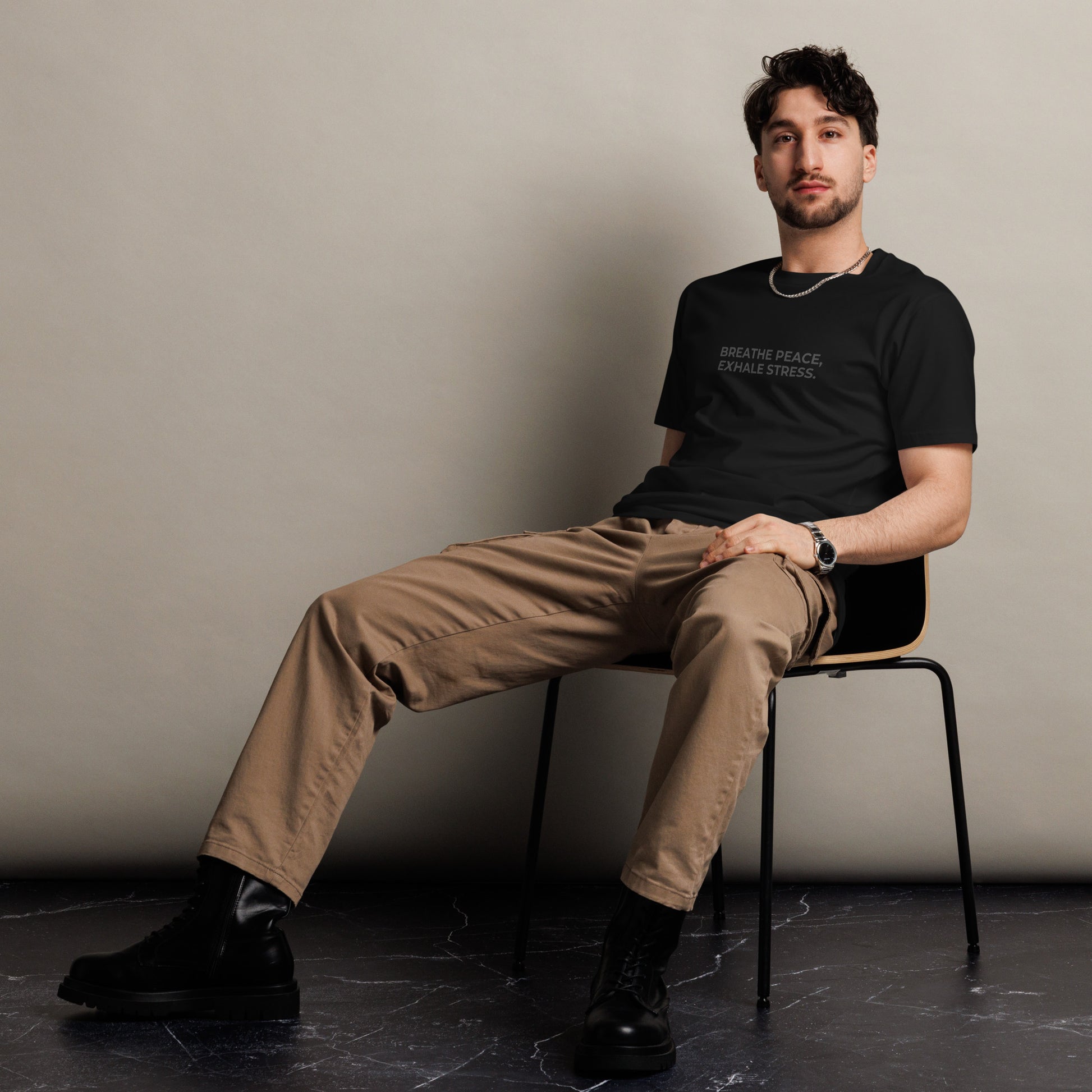 Man sitting wearing a black premium tee with the text "Breathe Peace, Exhale Stress".