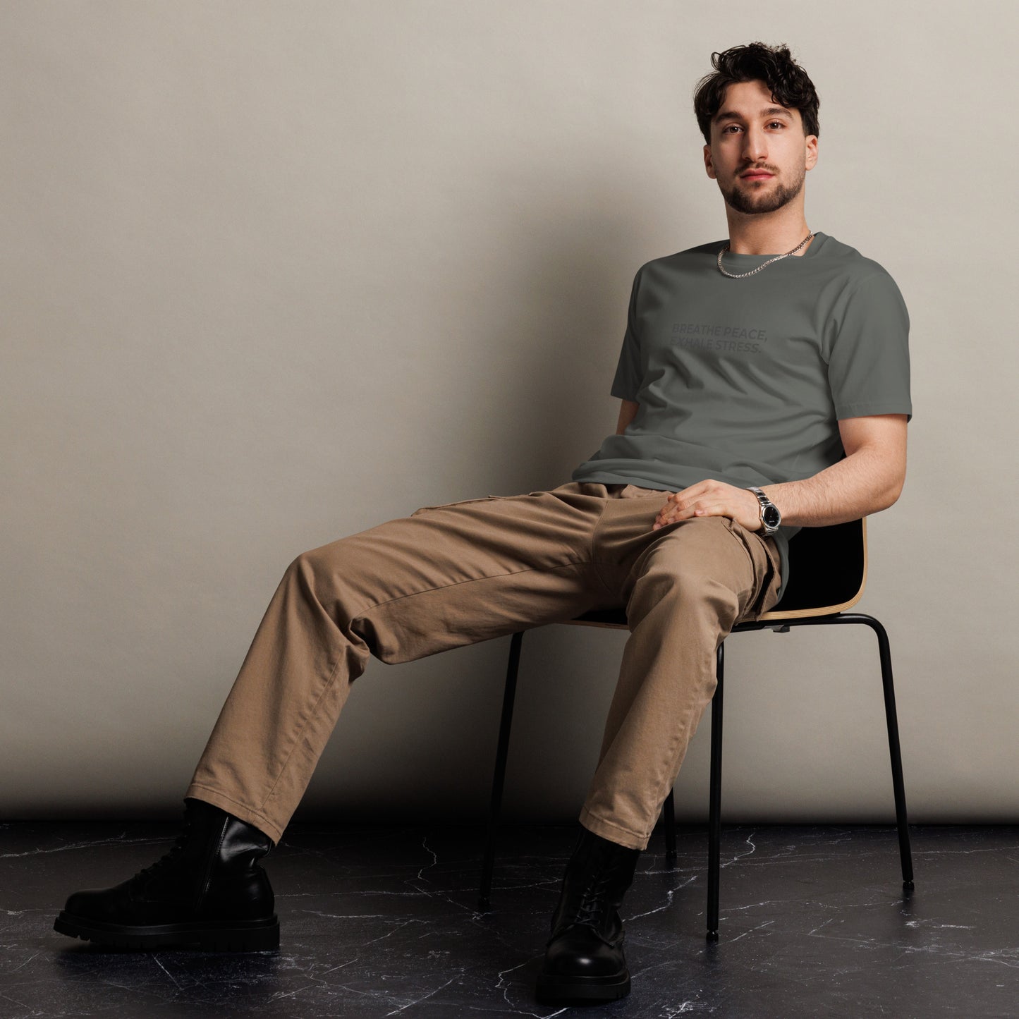 Man sitting wearing a charcoal premium tee with the text "Breathe Peace, Exhale Stress".