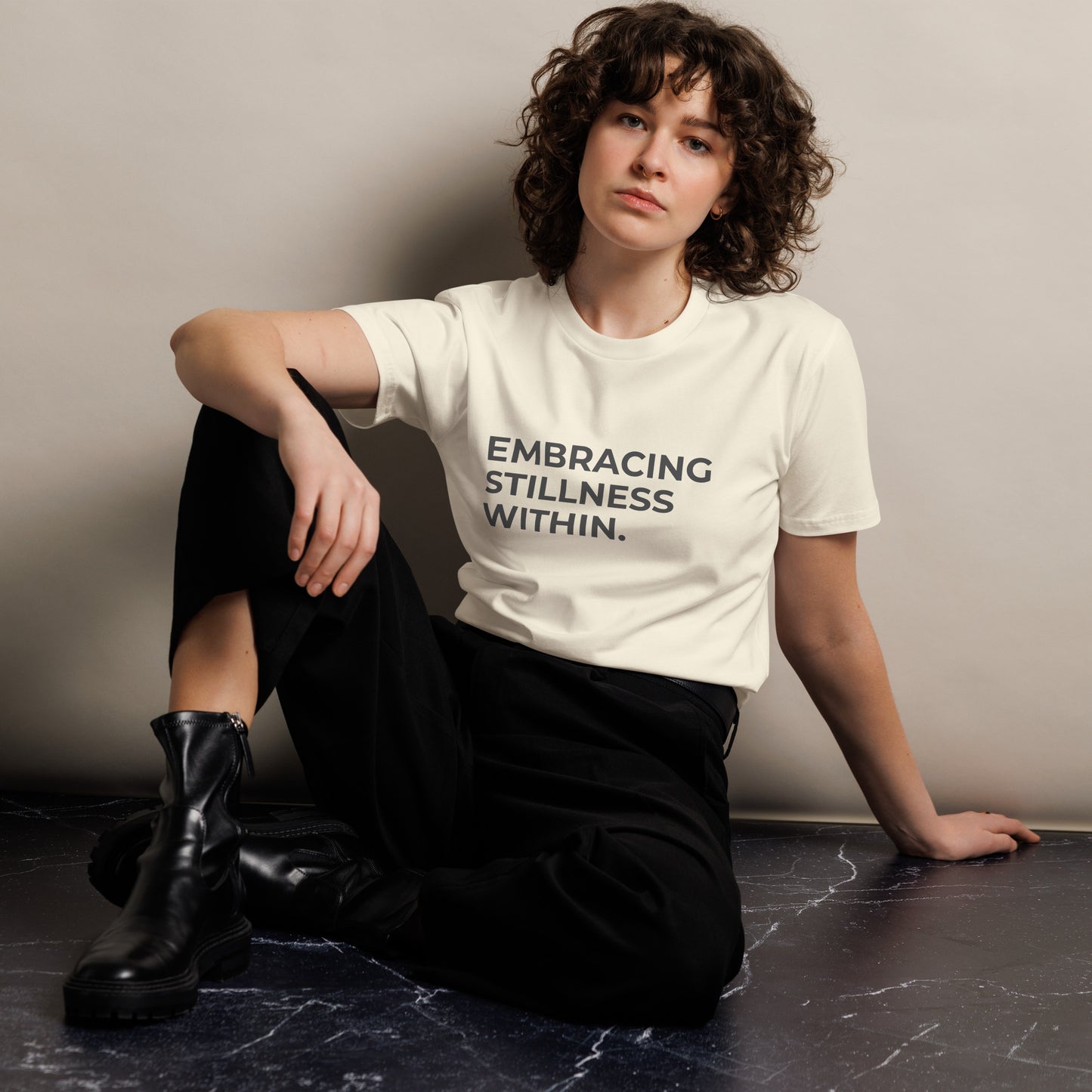 Woman wearing a natural premium tee with "Embracing Stillness Within" text.