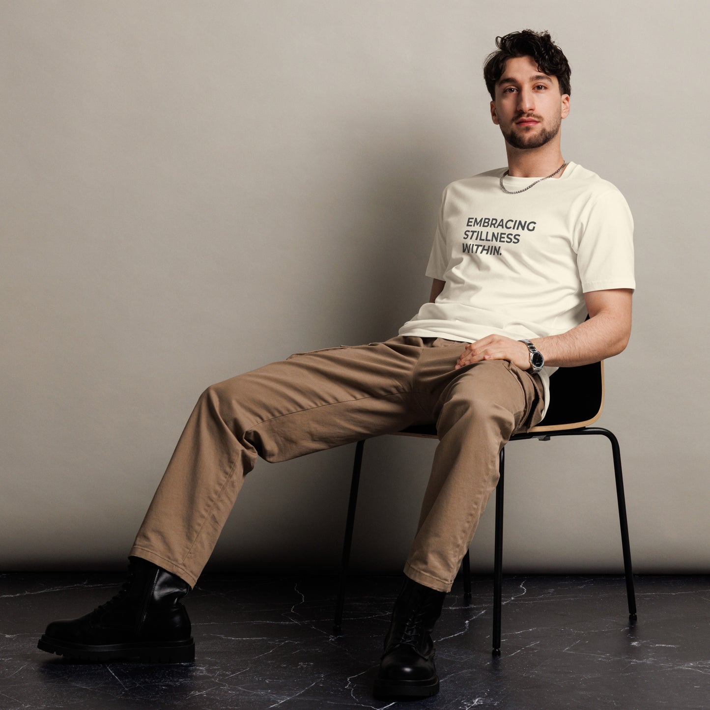 Man sitting wearing a natural premium tee with the text "Embracing Stillness Within".