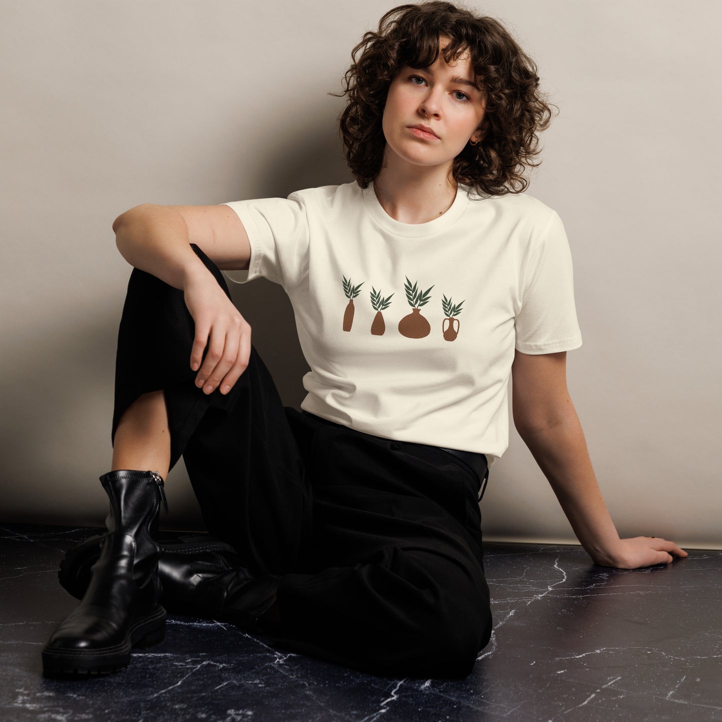 Woman wearing a natural t-shirt with abstract plant designs and color options in black, navy blue, green, gray, and white, available in sizes S to 3XL.