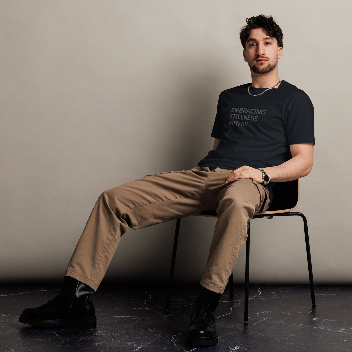 Man sitting wearing a navy premium tee with the text "Embracing Stillness Within".