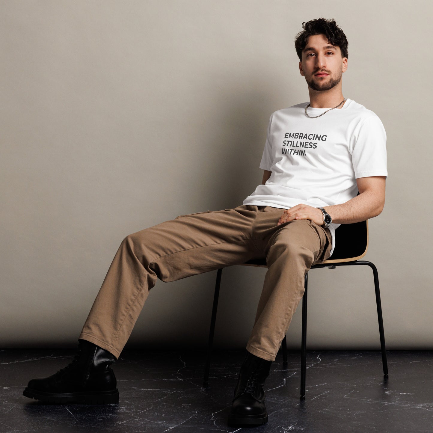 Man sitting wearing a white premium tee with the text "Embracing Stillness Within".