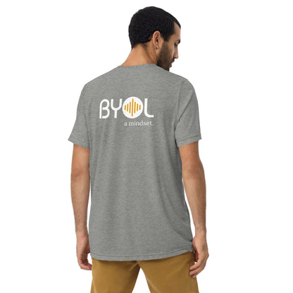 A young man with short dark hair wearing a grey tri-blend "BYOL: a mindset" T-shirt, viewed from the back. The T-shirt features the "BYOL" logo in white and yellow on the back and is available in multiple colors (black, red, gray, pink, beige, plus more) and sizes (S-3XL). The "be you out loud" logo is displayed at the top.