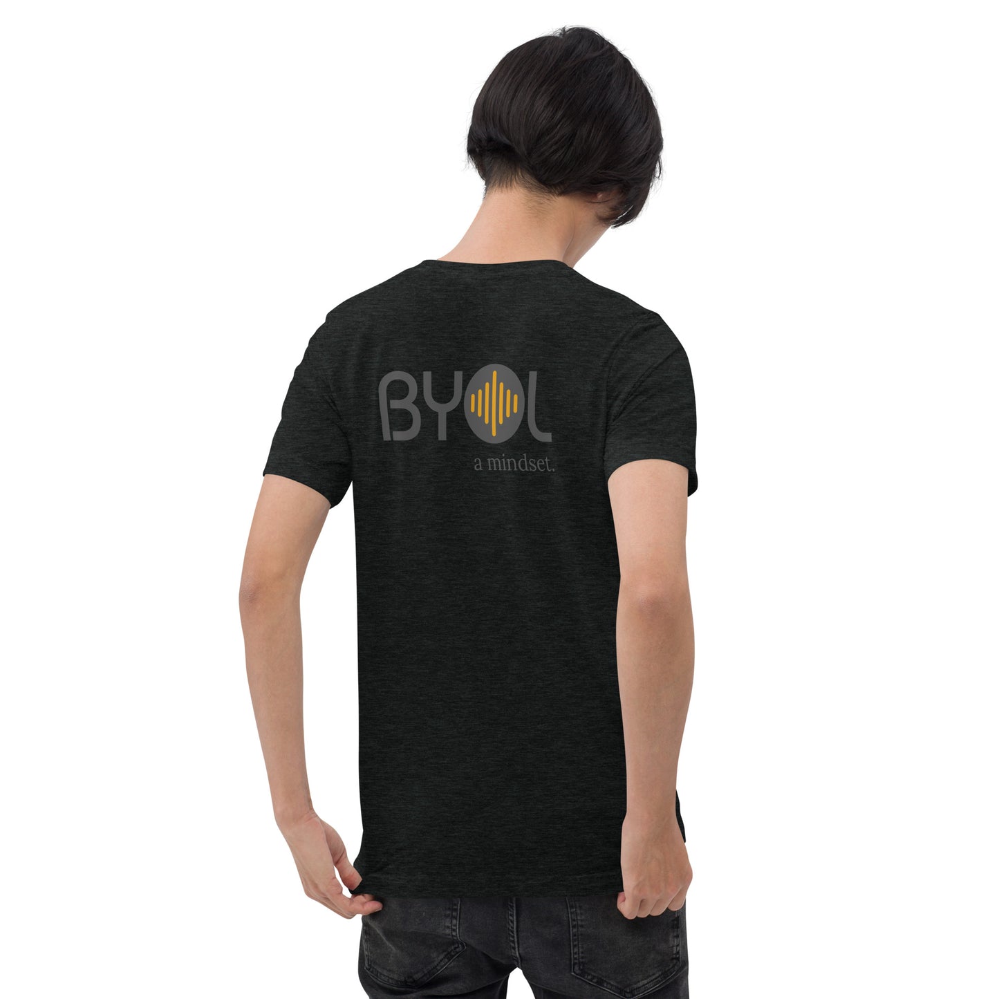 A young man with short black hair wearing a heather black tri-blend "BYOL: a mindset" T-shirt, viewed from the back. The T-shirt features the "BYOL" logo in black and yellow on the back and is available in multiple colors (black, red, gray, pink, gold, plus more) and sizes (S-3XL). The "be you out loud" logo is displayed at the top.