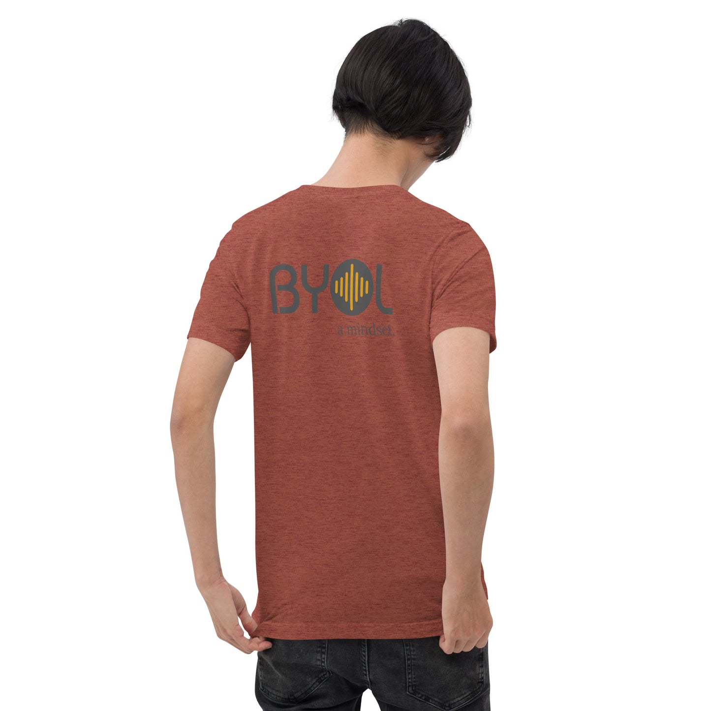 A young man with short black hair wearing a clay tri-blend "BYOL: a mindset" T-shirt, viewed from the back. The T-shirt features the "BYOL" logo in black and yellow on the back and is available in multiple colors (black, red, gray, pink, gold, plus more) and sizes (S-3XL). The "be you out loud" logo is displayed at the top.