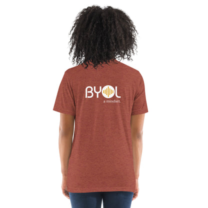 Back view of a woman wearing a clay triblend BYOL mindset t-shirt with color options in black, red, pink, gray, and yellow, available in sizes S to 3XL.