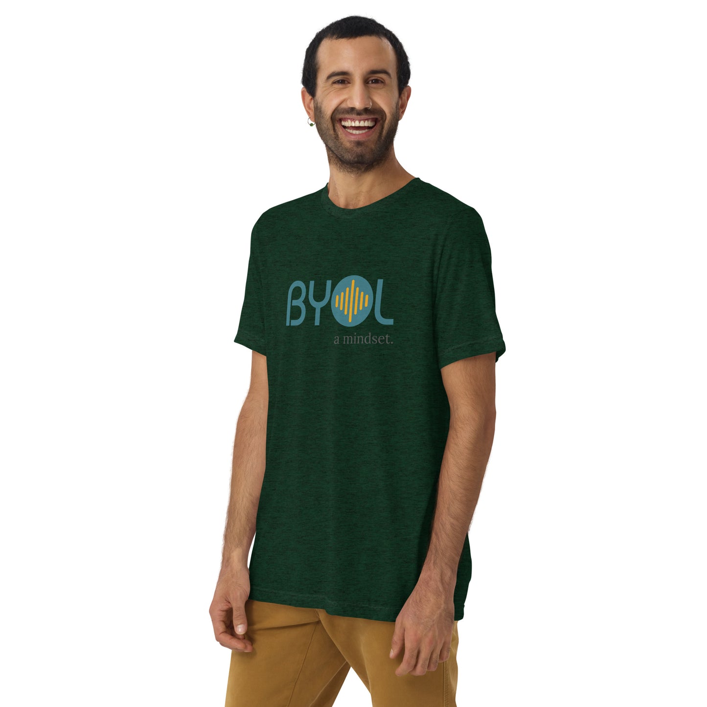 A young man with short dark hair and a beard wearing a emerald tri-blend "BYOL: a mindset" T-shirt, smiling and standing with his arms at his sides. The T-shirt features the "BYOL" logo in teal and is available in multiple colors (black, red, gray, pink, yellow, plus more) and sizes (S-3XL). The "be you out loud" logo is displayed at the top.