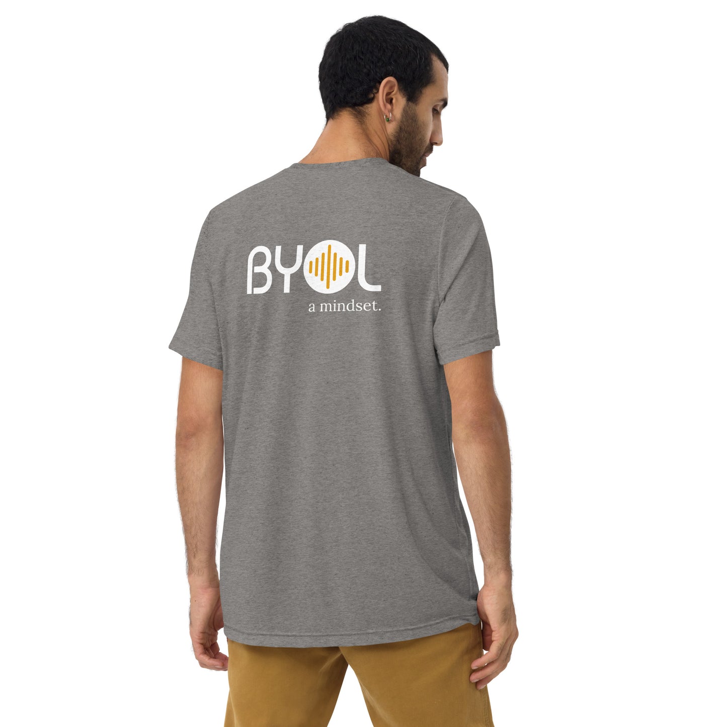 A young man with short dark hair wearing a grey tri-blend "BYOL: a mindset" T-shirt, viewed from the back. The T-shirt features the "BYOL" logo in white and yellow on the back and is available in multiple colors (black, red, gray, pink, beige, plus more) and sizes (S-3XL). The "be you out loud" logo is displayed at the top.