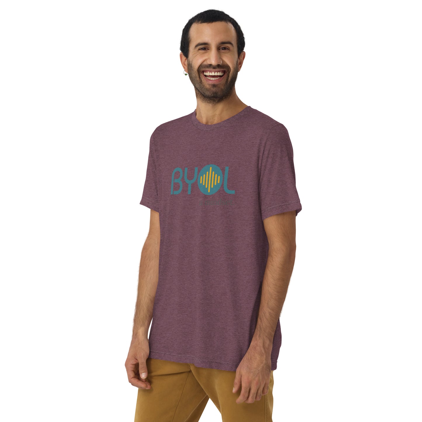 A young man with short dark hair and a beard wearing a purple tri-blend "BYOL: a mindset" T-shirt, smiling and standing with his arms at his sides. The T-shirt features the "BYOL" logo in teal and is available in multiple colors (black, red, gray, pink, yellow, plus more) and sizes (S-3XL). The "be you out loud" logo is displayed at the top.