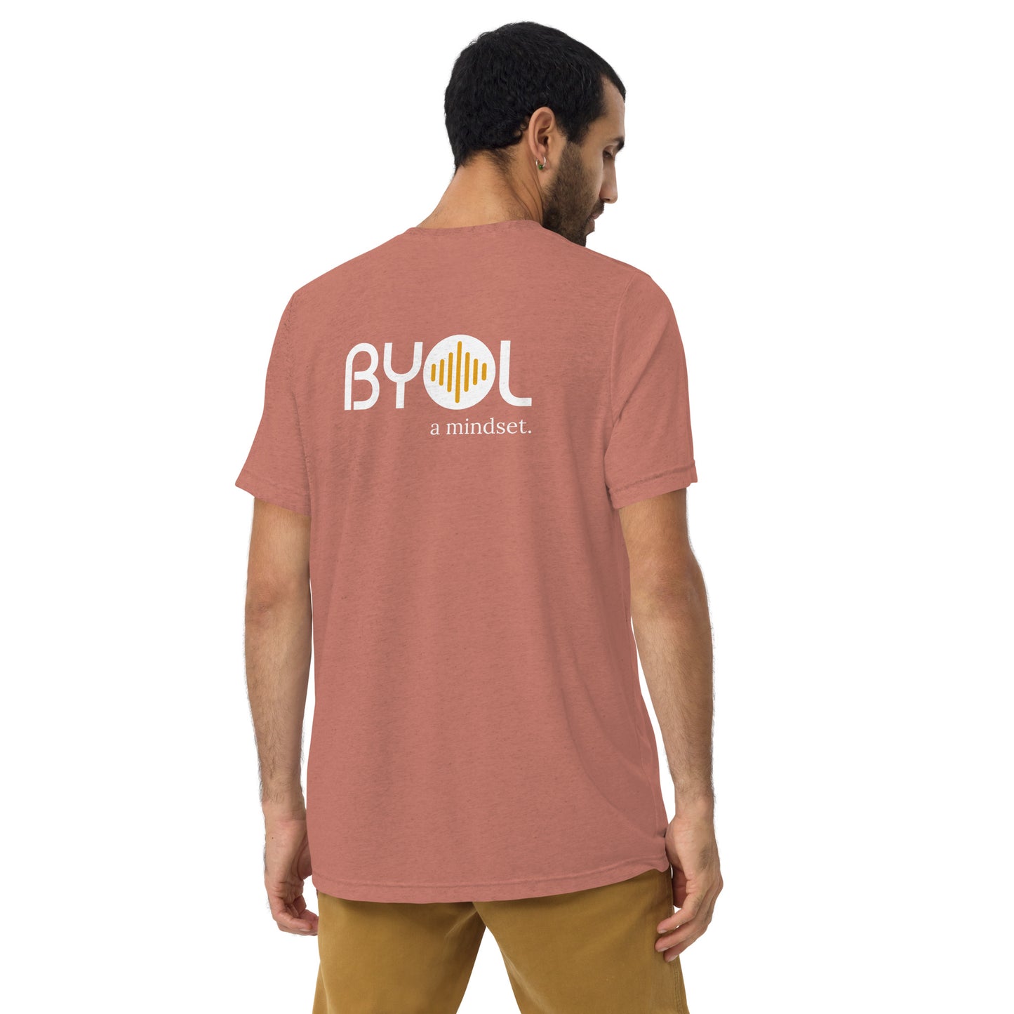 A young man with short dark hair wearing a mauve tri-blend "BYOL: a mindset" T-shirt, viewed from the back. The T-shirt features the "BYOL" logo in white and yellow on the back and is available in multiple colors (black, red, gray, pink, beige, plus more) and sizes (S-3XL). The "be you out loud" logo is displayed at the top.