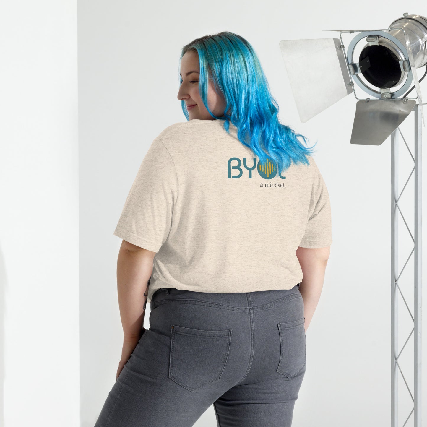 Back view of a woman wearing a natural tri-blend BYOL mindset t-shirt with color options in black, red, pink, gray, and yellow, available in sizes S to 3XL.