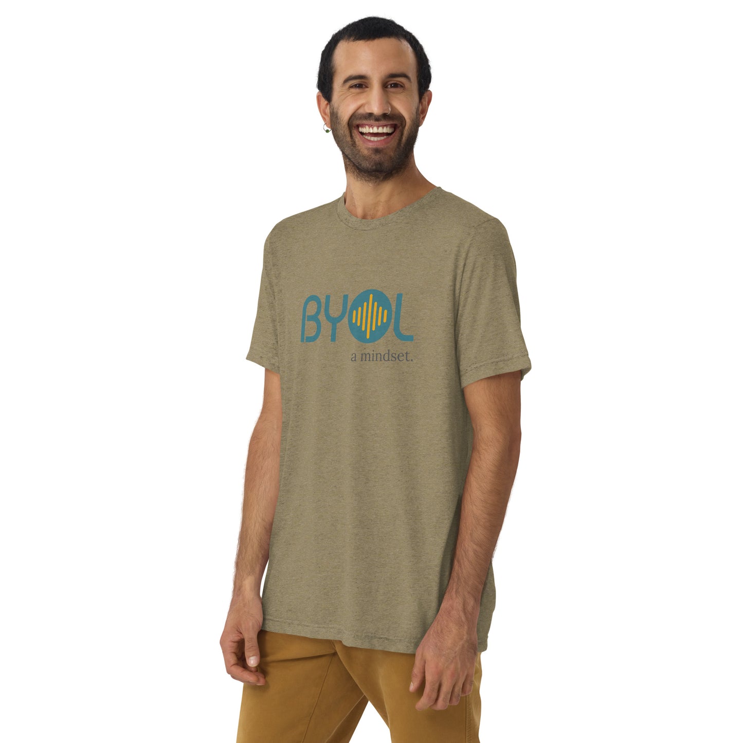 A young man with short dark hair and a beard wearing a olive green tri-blend "BYOL: a mindset" T-shirt, smiling and standing with his arms at his sides. The T-shirt features the "BYOL" logo in teal and is available in multiple colors (black, red, gray, pink, yellow, plus more) and sizes (S-3XL). The "be you out loud" logo is displayed at the top.