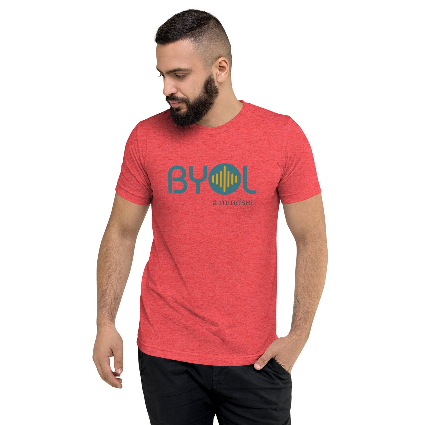 A young man with short dark hair and a beard wearing a red tri-blend "BYOL: a mindset" T-shirt, standing with one hand in his pocket and looking down. The T-shirt features the "BYOL" logo in blue and yellow on the front and is available in multiple colors (black, red, gray, pink, gold, plus more) and sizes (S-3XL). The "be you out loud" logo is displayed at the top.