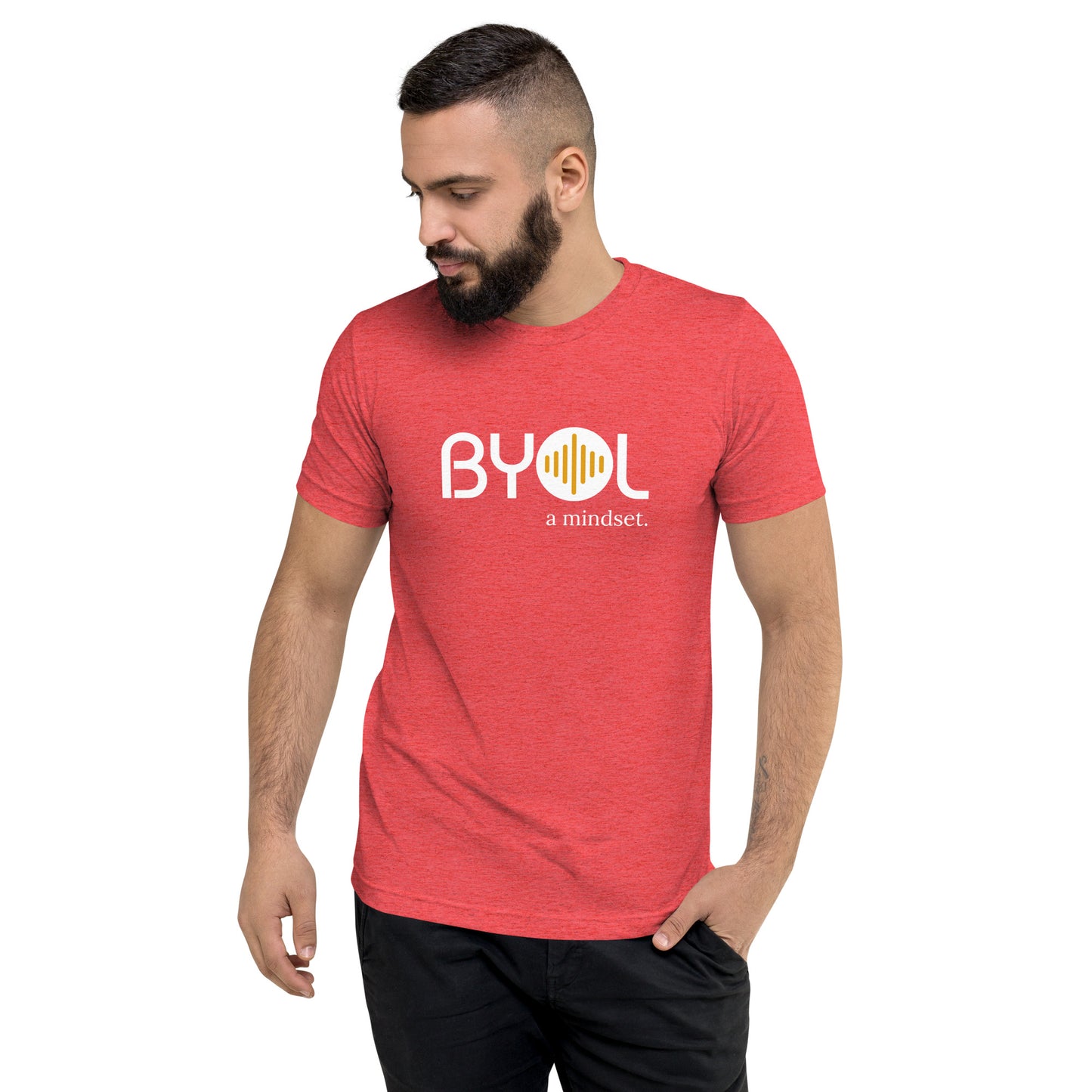 A young man with short dark hair and a beard wearing a red tri-blend "BYOL: a mindset" T-shirt, standing with one hand in his pocket and looking down. The T-shirt features the "BYOL" logo in white and yellow on the front and is available in multiple colors (black, red, gray, pink, gold, plus more) and sizes (S-3XL). The "be you out loud" logo is displayed at the top.