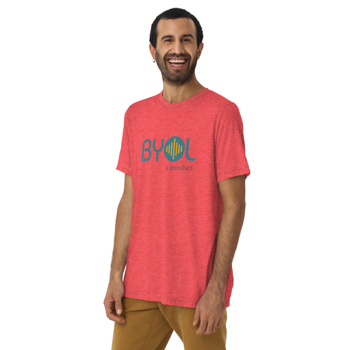 A young man with short dark hair and a beard wearing a red tri-blend "BYOL: a mindset" T-shirt, smiling and standing with his arms at his sides. The T-shirt features the "BYOL" logo in teal and is available in multiple colors (black, red, gray, pink, yellow, plus more) and sizes (S-3XL). The "be you out loud" logo is displayed at the top.