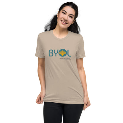 Woman wearing a tan triblend BYOL mindset t-shirt with color options in black, red, pink, gray, and yellow, available in sizes S to 3XL.