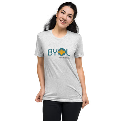 Woman wearing a white fleck triblend BYOL mindset t-shirt with color options in black, red, pink, gray, and yellow, available in sizes S to 3XL.