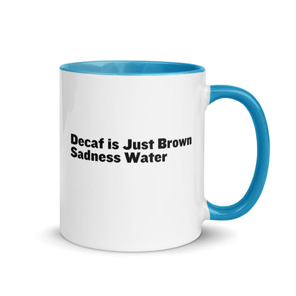 White ceramic mug with a light blue inside and handle with the words, "Decaf is just Brown Sadness water"