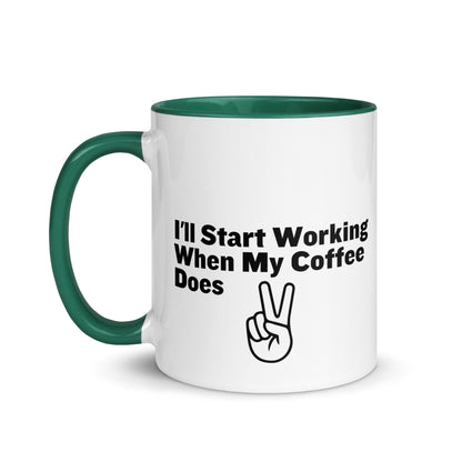 White ceramic mug with a green inside and handle with the words, "I'll start working when my coffee does"