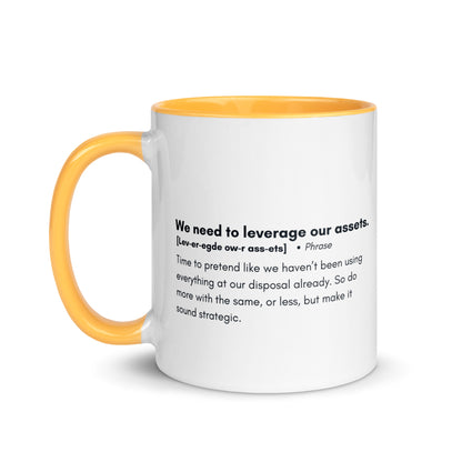 White ceramic mug with golden yellow inside and handle with the words, "We need to leverage our assets" followed by a humorous definition.