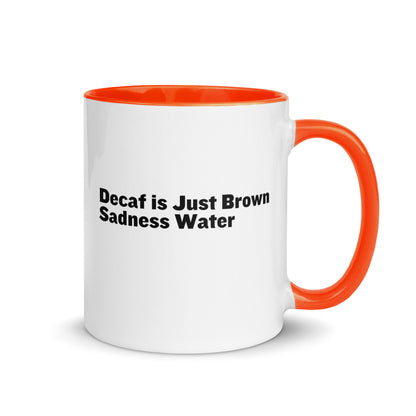 White ceramic mug with a orange inside and handle with the words, "Decaf is just Brown Sadness water"