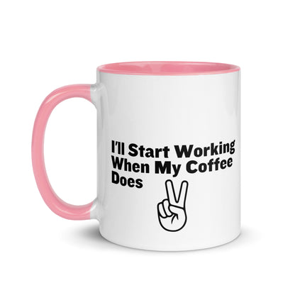 White ceramic mug with a pink inside and handle with the words, "I'll start working when my coffee does"