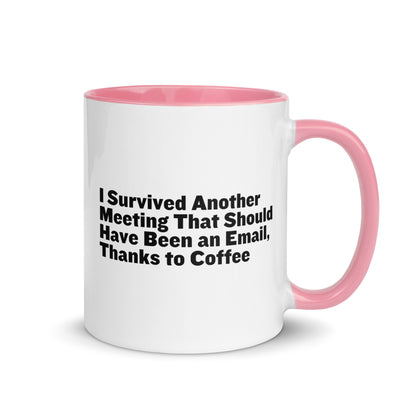 White ceramic mug with pink inside and on the handle with words that say, "I survived another meeting that should have been an email, thanks to coffee"