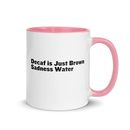 White ceramic mug with a pink inside and handle with the words, "Decaf is just Brown Sadness water"