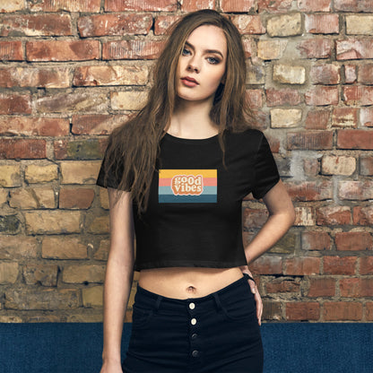 Confident young woman showcasing the Women's Retro 'Good Vibes' Black Crop Top by Be You Out Loud, against a rustic brick backdrop.