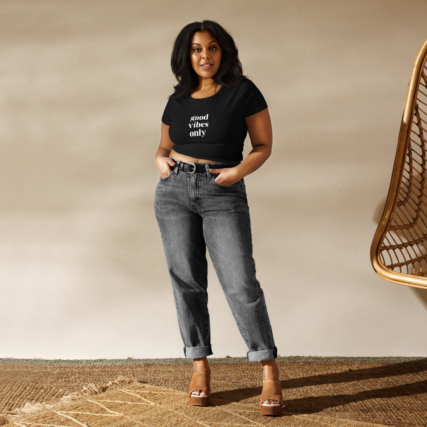 Confident woman wearing a slim-fit black crop top with 'good vibes only' printed text, paired with grey high-waisted jeans.