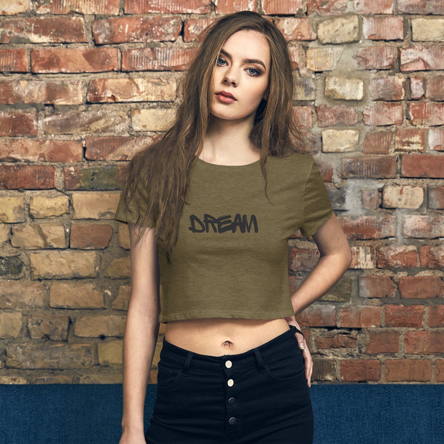 Model wearing Women's 'DREAM' Inspirational Heather Olive Crop Top  against a brick wall, embodying self-expression and motivation.