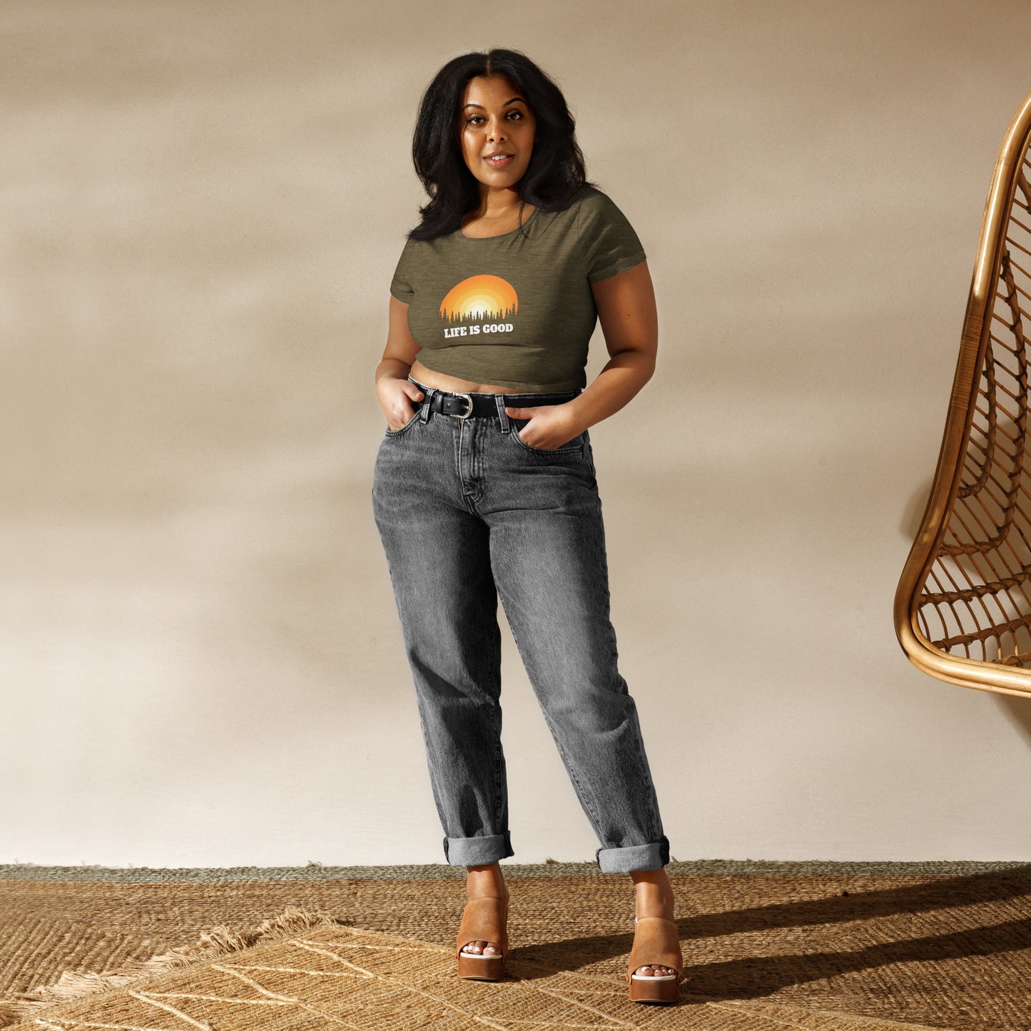 Confident woman wearing a heathered green inspirational crop top with a sunrise design and "Life Is Good" message, conveying positivity.