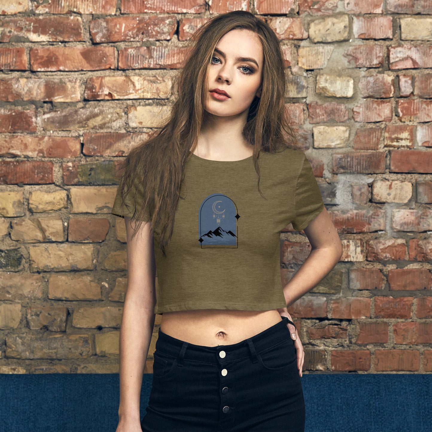 A woman wearing olive green black a slim fit crop top with a mountain and night sky design. 