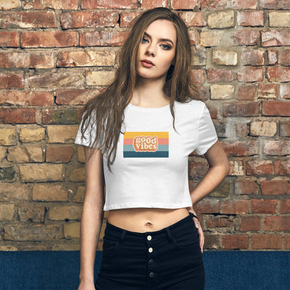 Confident young woman showcasing the Women's Retro 'Good Vibes' White Crop Top by Be You Out Loud, against a rustic brick backdrop.