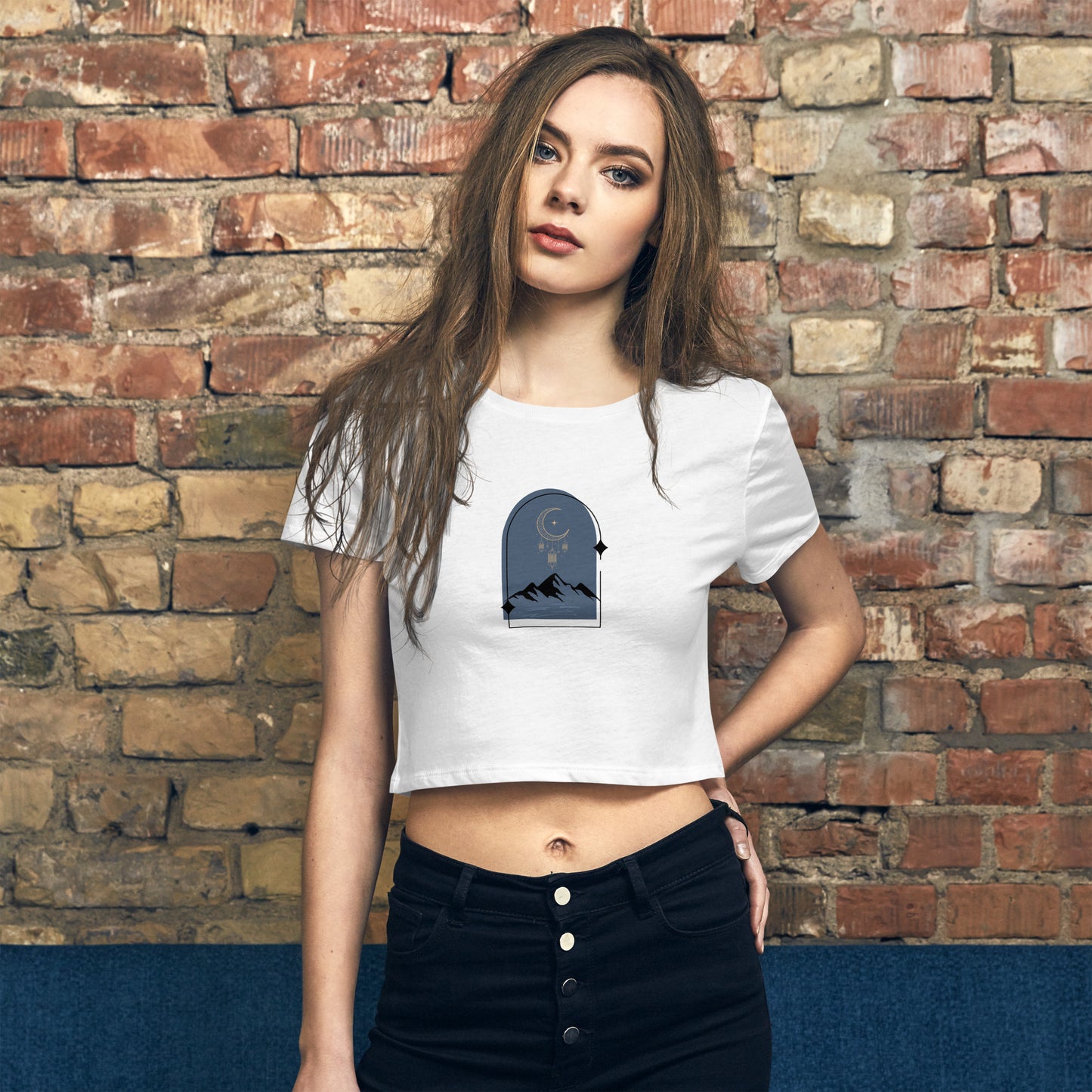 A woman wearing a white black a slim fit crop top with a mountain and night sky design. 