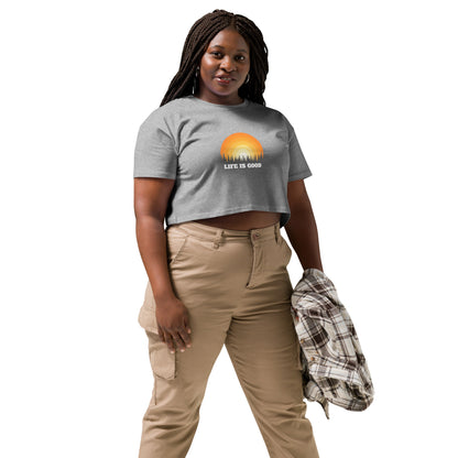 Woman in a athletic grey crop top with a "Life is Good" sunset graphic, pairing it with khaki pants and a casual jacket.