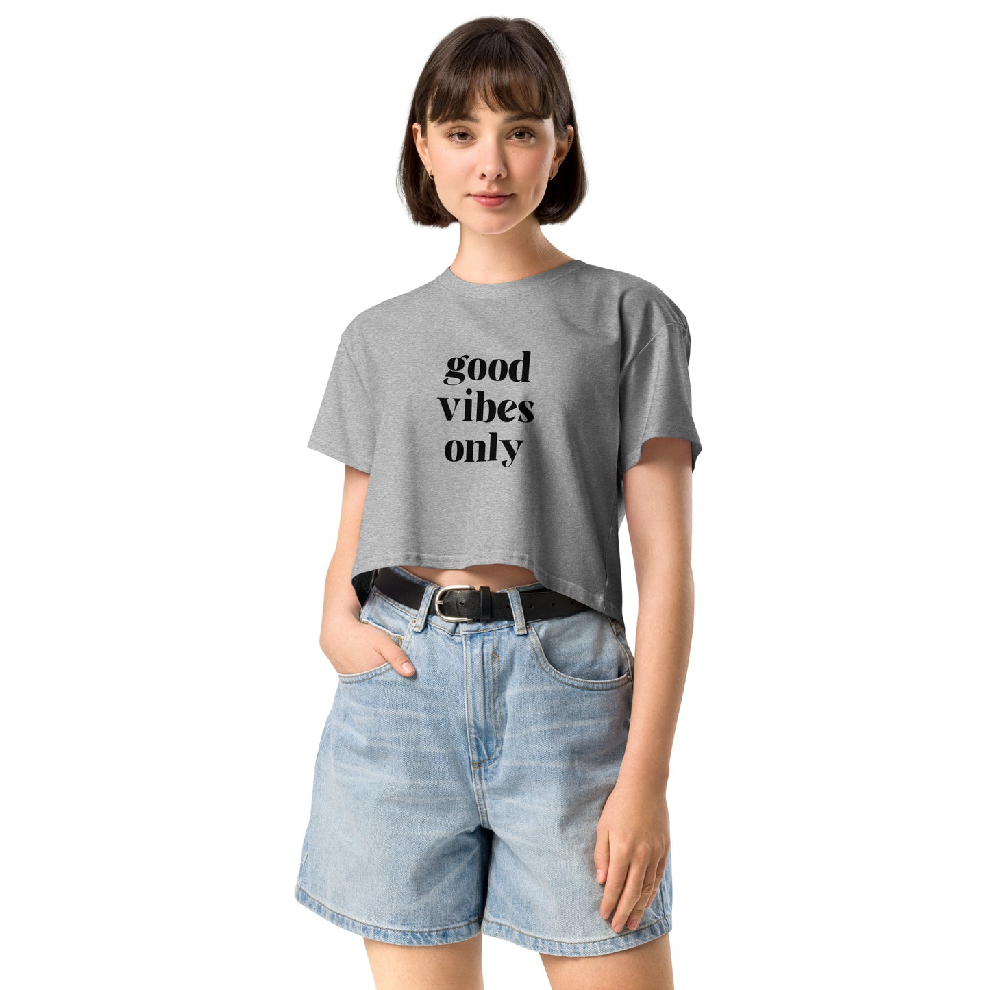 Content woman in a atheltic grey crop top with 'good vibes only' text, coupled with light blue denim shorts, conveying a laid-back style.