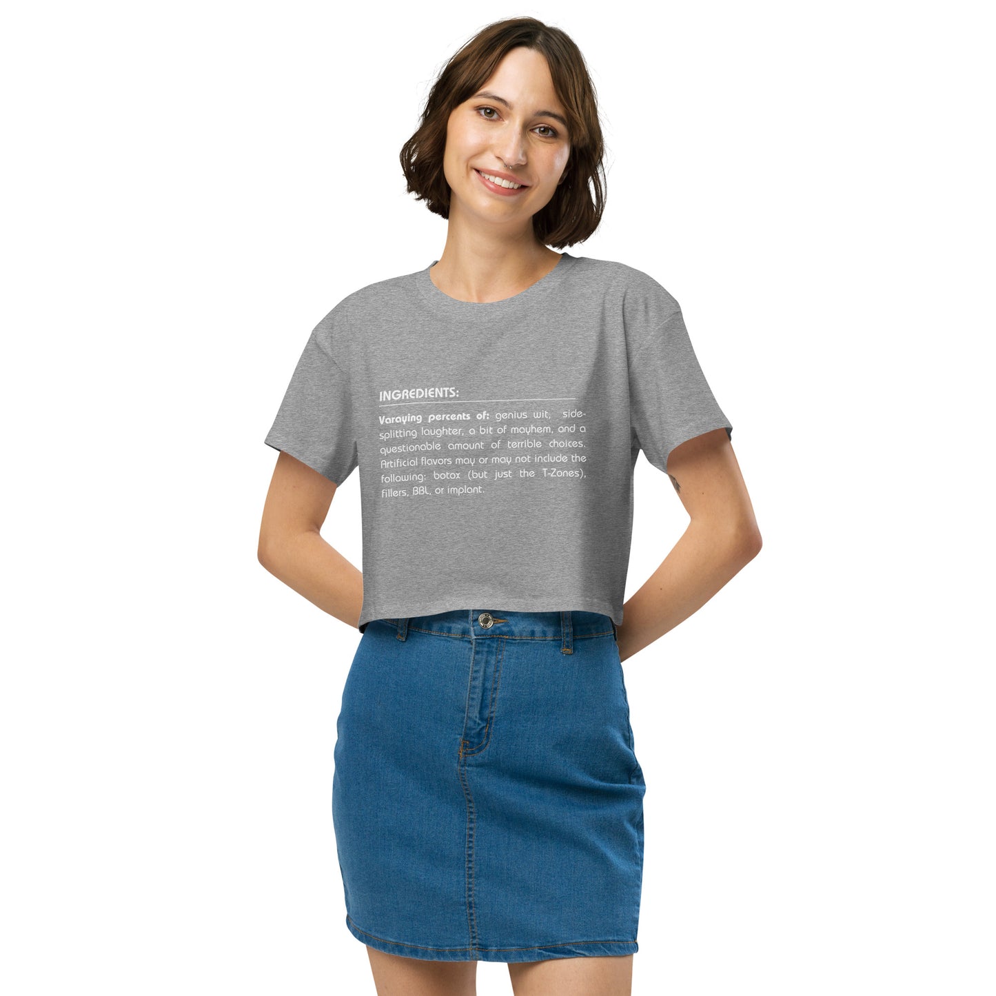 Cheerful woman in a grey crop top featuring a quirky 'Ingredients' list, paired with a denim skirt for a look that combines fun and trendy style.