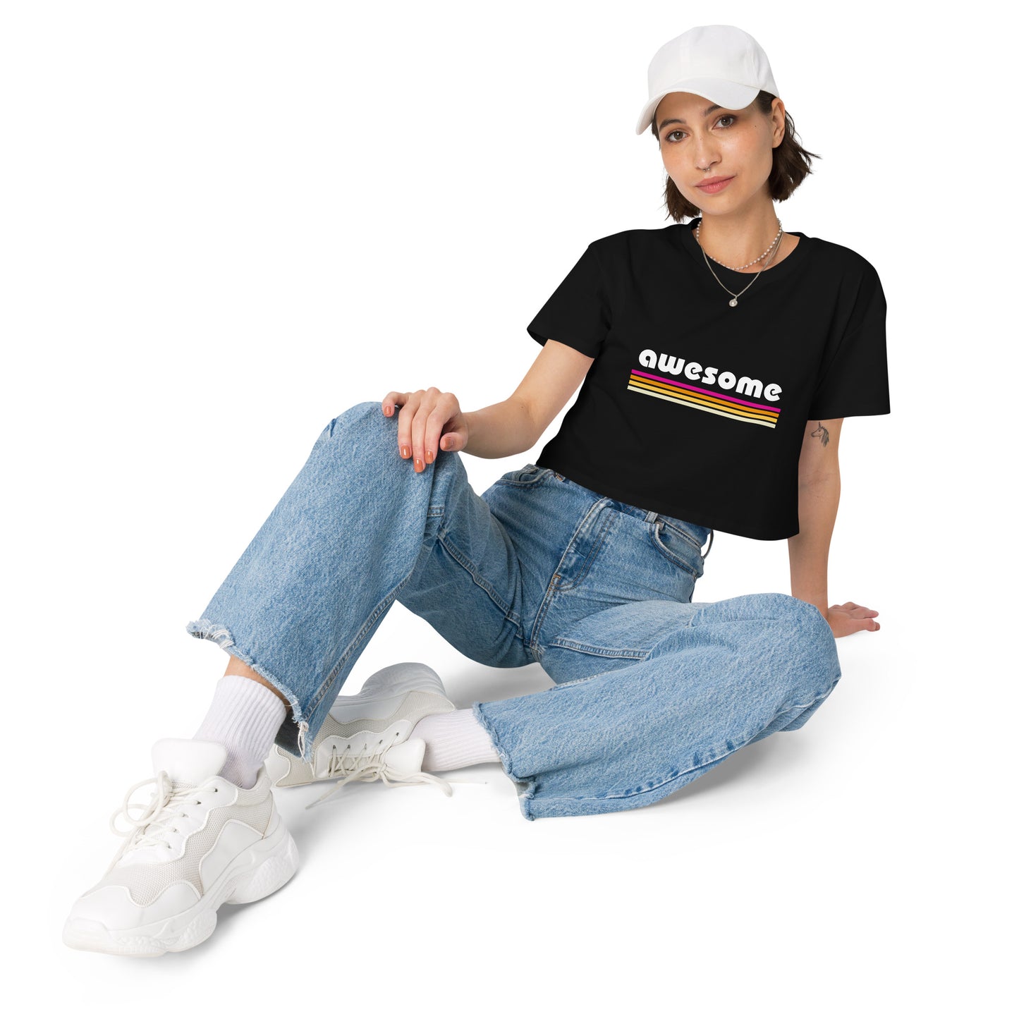 Casual woman in a black retro-styled crop top with 'Awesome' in rainbow stripes sitting with wide-leg jeans and white sneakers