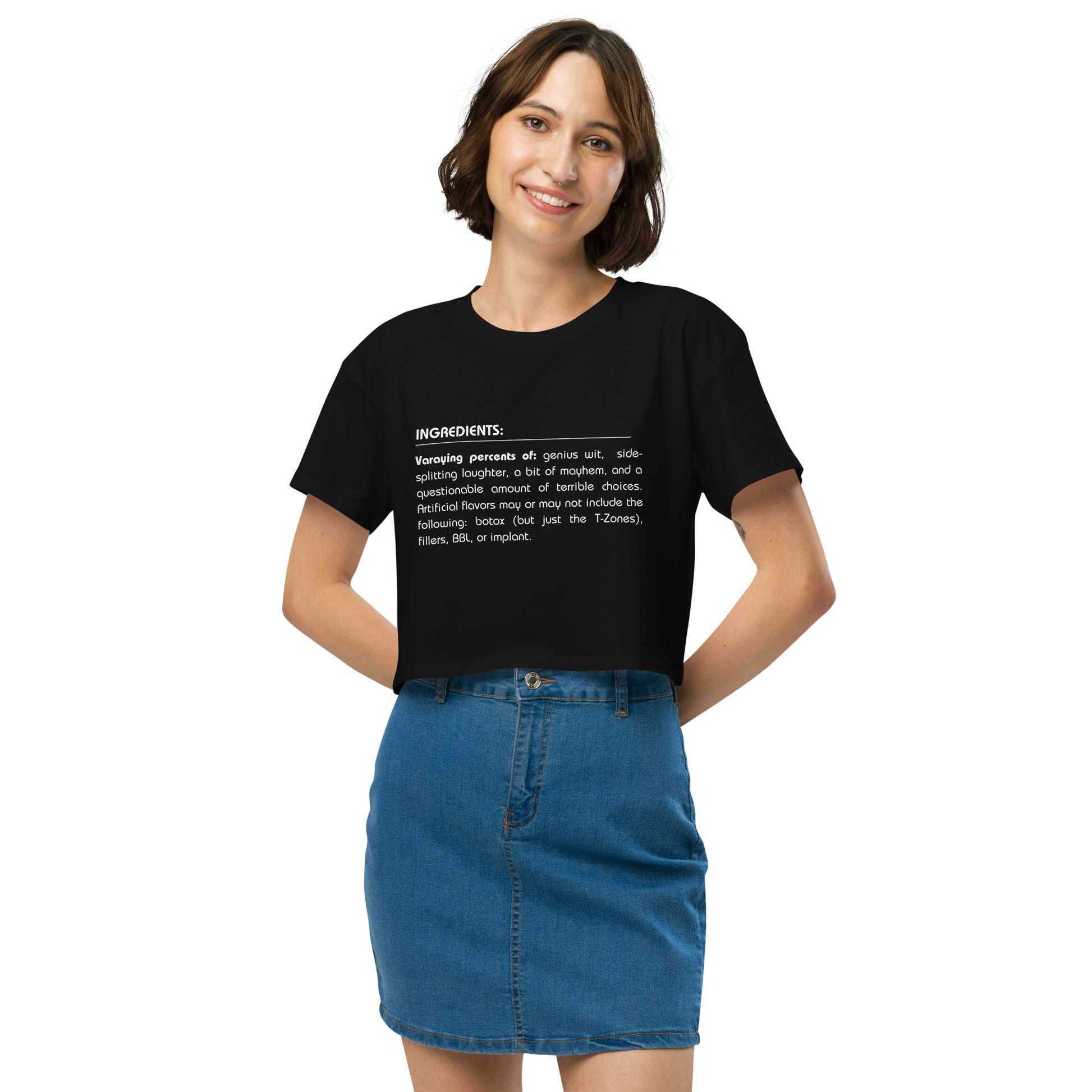 Cheerful woman in a black crop top featuring a quirky 'Ingredients' list, paired with a denim skirt for a look that combines fun and trendy style.