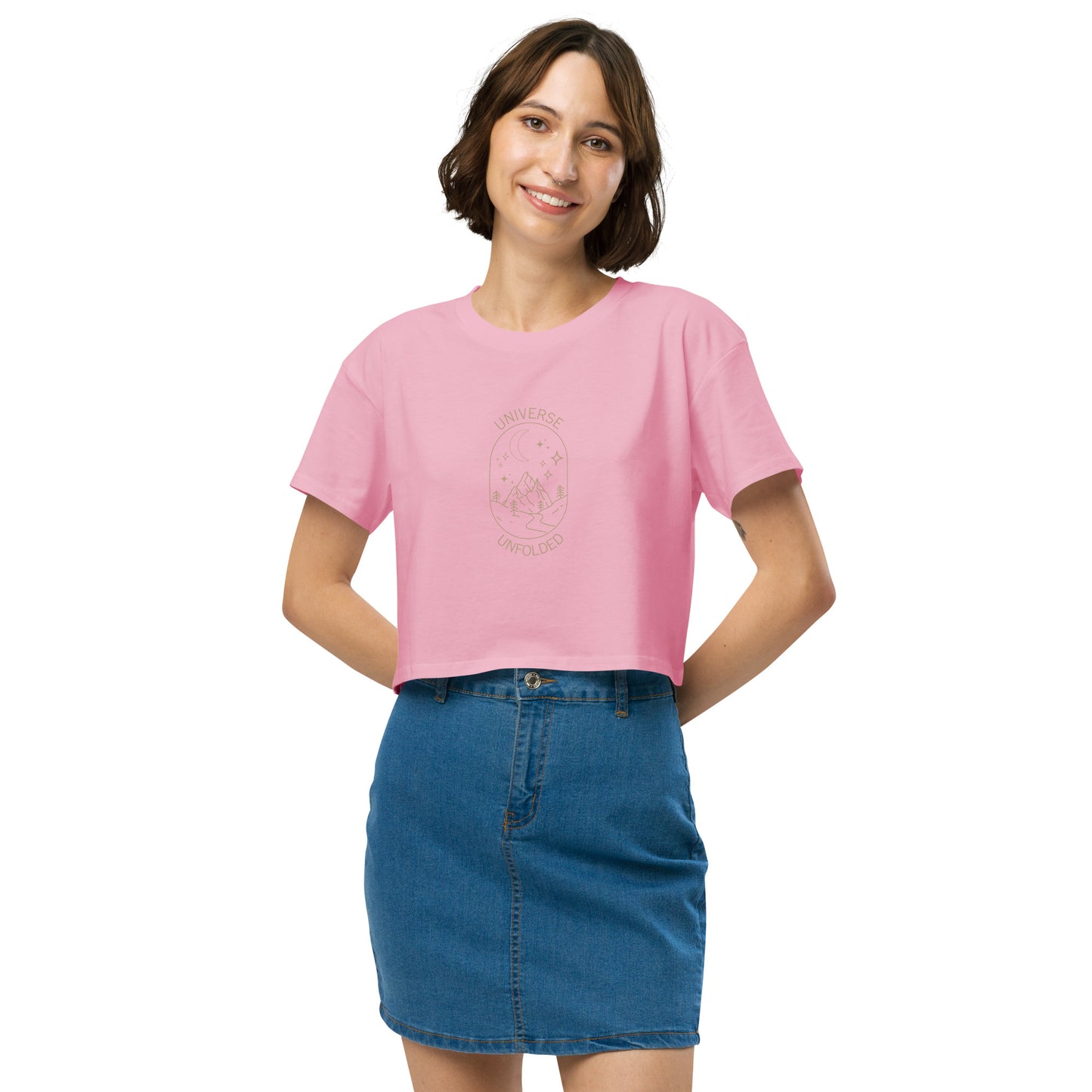 Cheerful woman in a bubblegum pink crop top with 'UNIVERSE UNFOLDER' and celestial design, paired with a denim skirt.