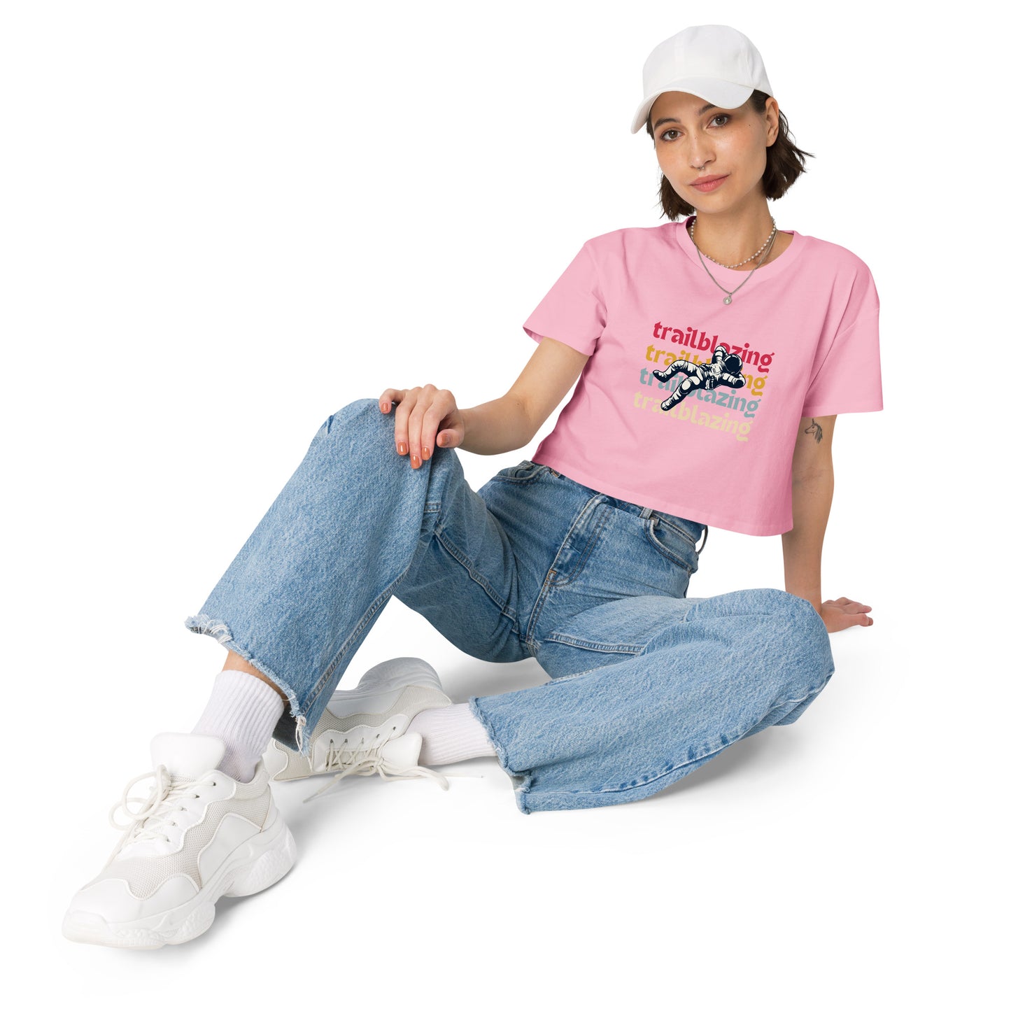 Relaxed woman in a bubblegum pink crop top with a trailblazing graphic, paired with baggy denim jeans and white sneakers, ready to make a statement.