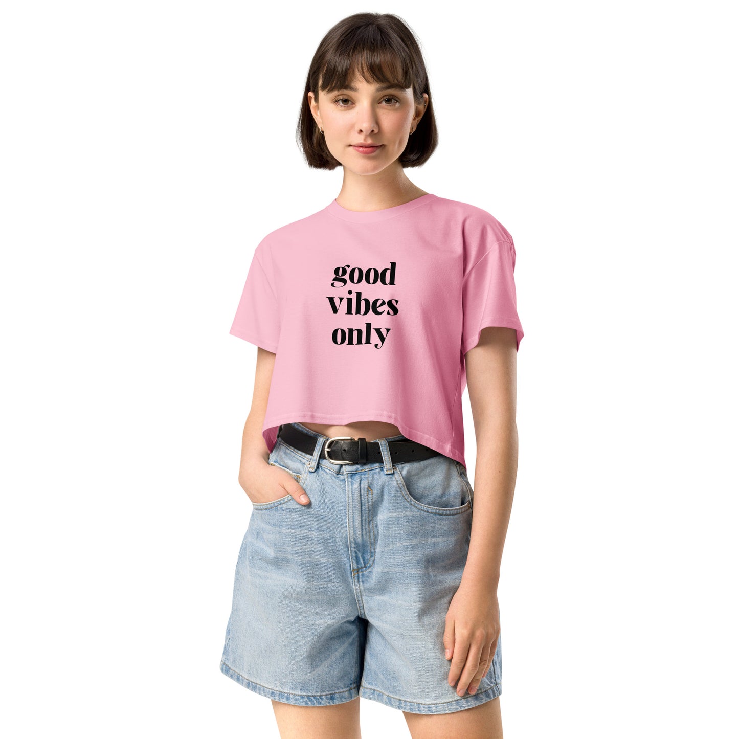 Woman wearing a bubblegum pink loose-fit crop top with 'good vibes only' slogan, paired with denim shorts, showcasing color and size options.