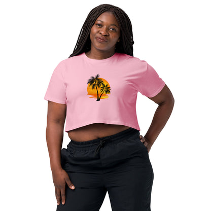 Smiling woman in a bubblegum pink crop top featuring a palm tree silhouette against a sunset, paired with casual black trousers for a laid-back, tropical-inspired look.