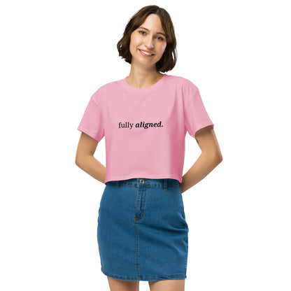 Woman wearing a bubblegum pink cropped t-shirt with the phrase "fully aligned" printed in black, smiling and posing against a clean background. Available in various colors: black, brown, pink, green, and white. Sizes range from XS to XL.