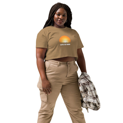 Woman in a camel crop top with a "Life is Good" sunset graphic, pairing it with khaki pants and a casual jacket.