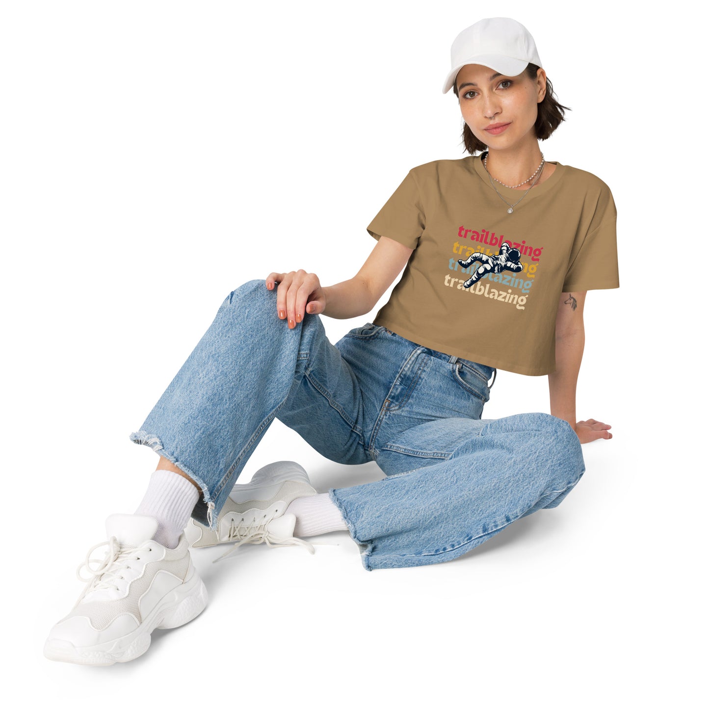 Relaxed woman in a camel crop top with a trailblazing graphic, paired with baggy denim jeans and white sneakers, ready to make a statement.