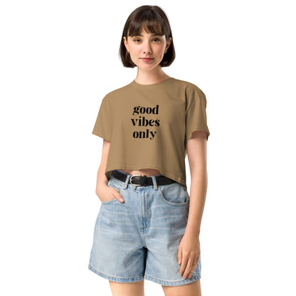 Content woman in a camel crop top with 'good vibes only' text, coupled with light blue denim shorts, conveying a laid-back style.